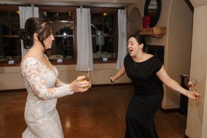 Two people dancing together in a ballroom setting with white curtains and wooden floors in the background.