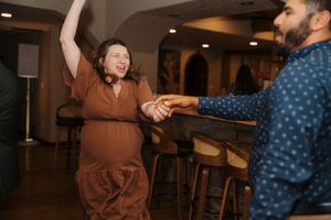 Two people dance together in a dimly lit room while others watch from the background.