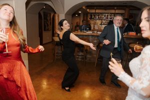 People dancing together at a social gathering in an indoor venue with warm lighting and wood floors.