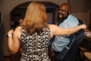 A couple dancing together in a dimly lit room, with the woman wearing a patterned dress and the man in blue.
