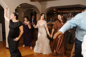 Wedding guests dance and celebrate on a wooden dance floor during an indoor reception celebration.