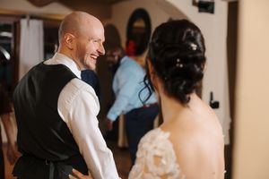 A couple shares a joyful laugh during their wedding reception while surrounded by guests.
