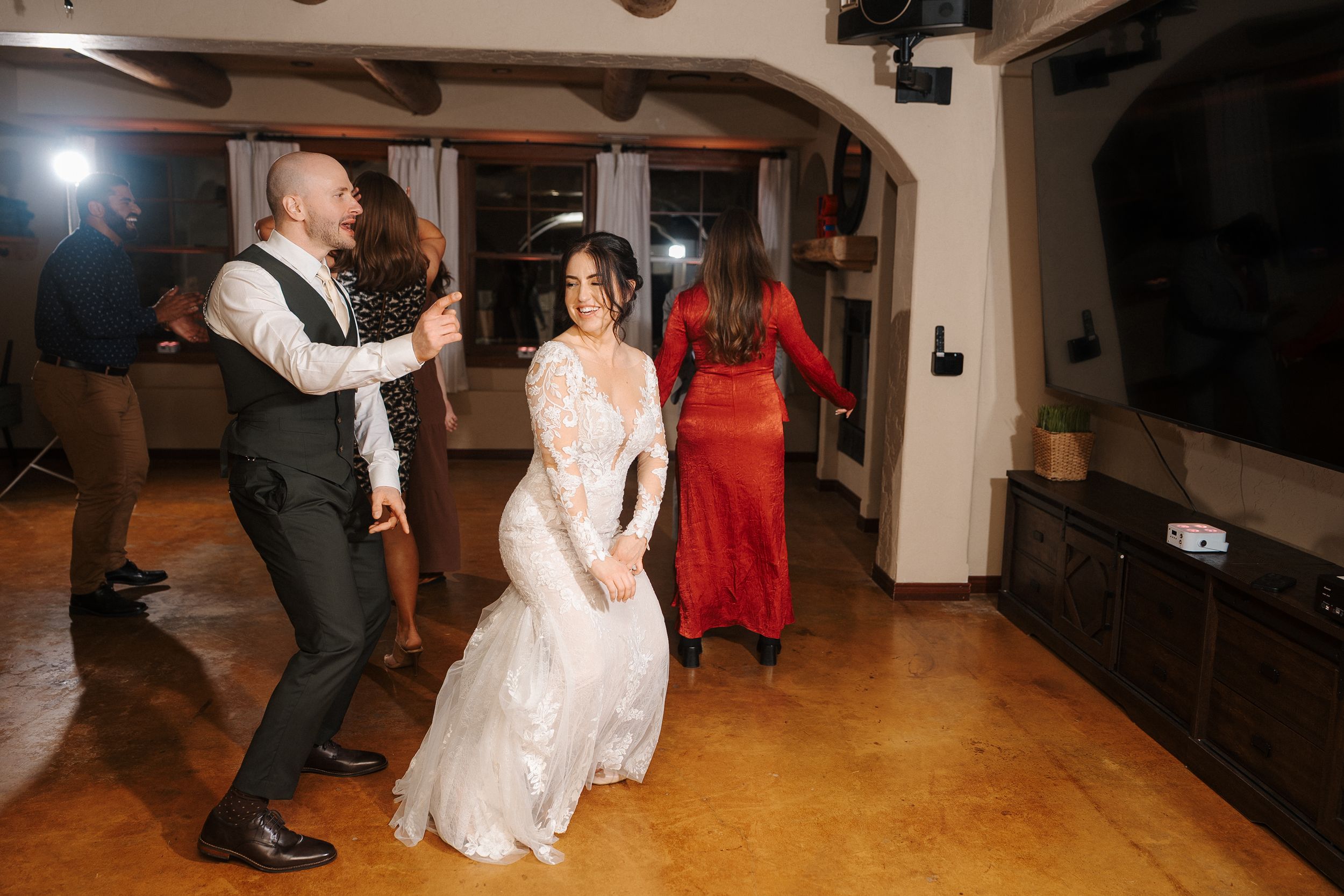 People dancing together at a wedding reception on a wooden dance floor with warm lighting.