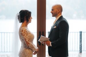 Wedding couple reading vows to each other in front of large windows with snowy landscape outside.