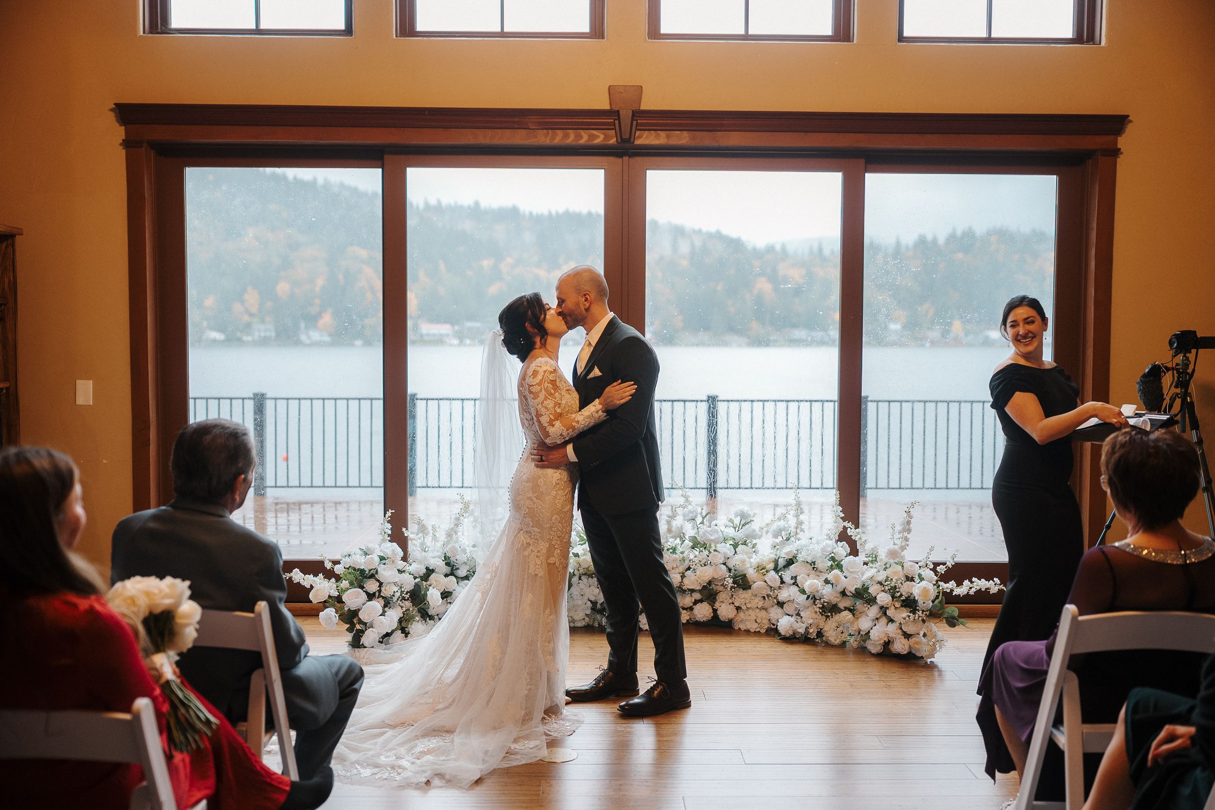 Wedding couple dances together in an elegant venue with floor-to-ceiling windows overlooking a scenic waterfront view.