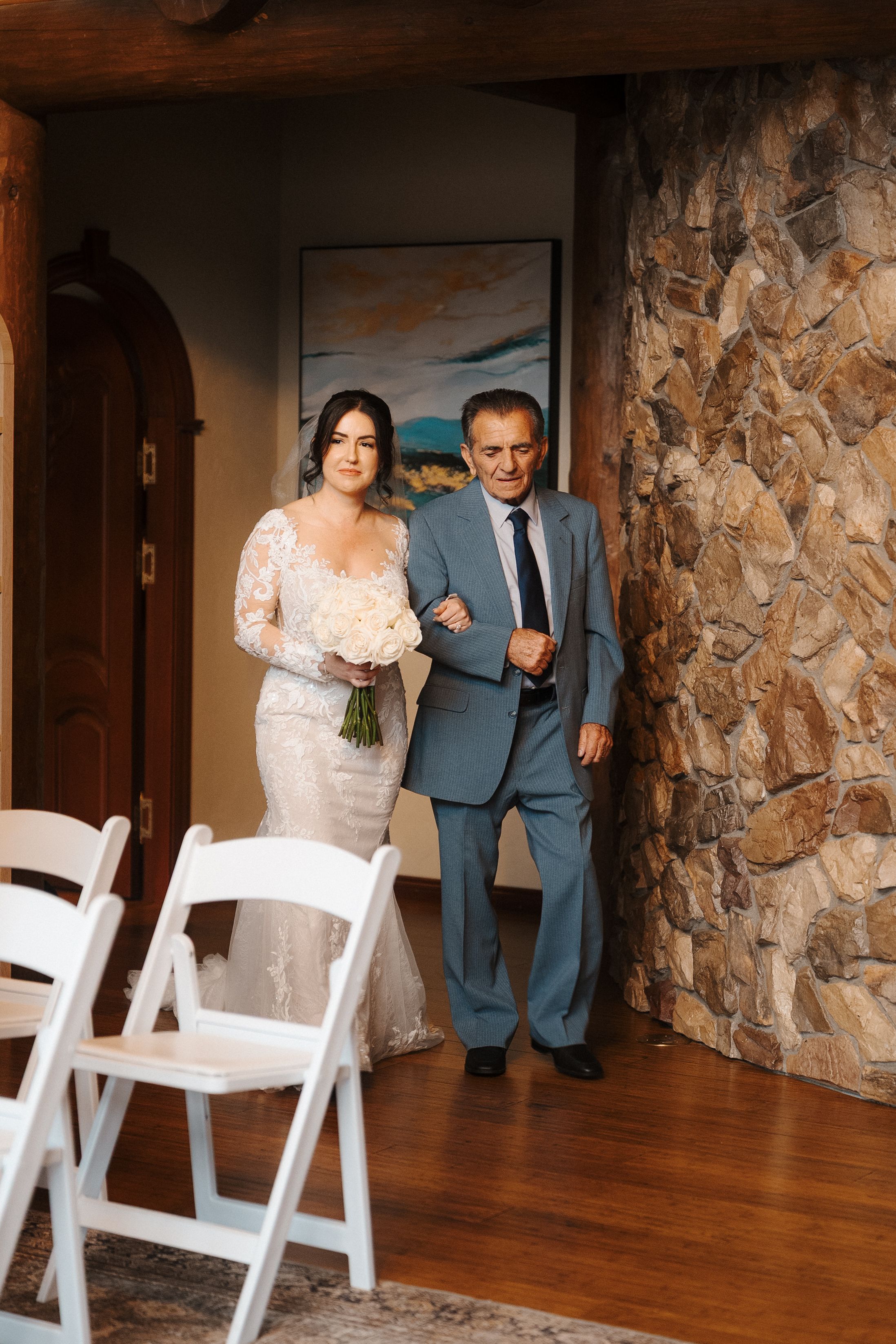 A wedding ceremony entrance with white folding chairs and stone walls in an elegant indoor venue.