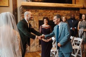 Wedding ceremony guests seated in white chairs with stone wall backdrop and floral arrangements.