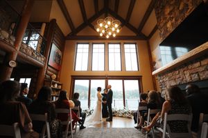Rustic wedding ceremony venue with wooden beams, stone walls and large windows illuminated by warm chandelier lighting.