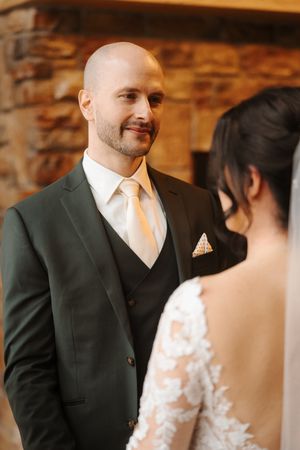A bride and groom share an intimate moment during their wedding ceremony in a rustic brick-walled venue.
