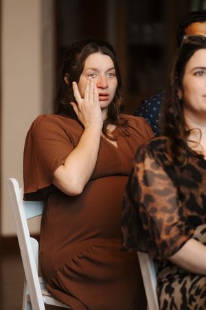 Two people sit together on white chairs, one wearing a brown sweater and the other in a patterned top.