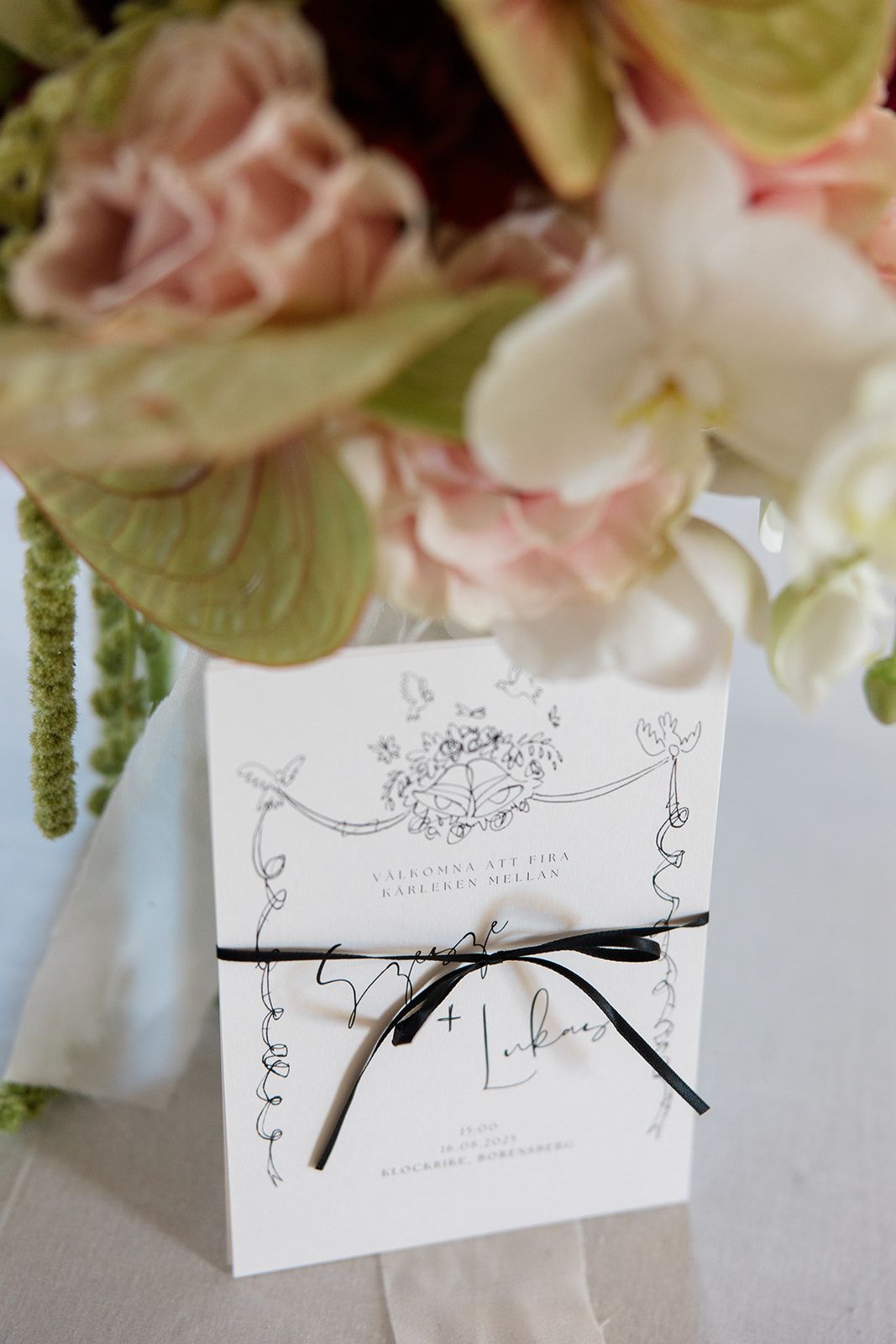 Black and white illustrated place cards with floral designs sit alongside pink and white flowers on a light gray surface.