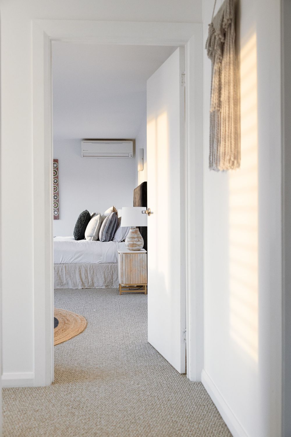 Minimalist white bedroom interior with beige carpet and natural light streaming through windows creating a serene atmosphere.
