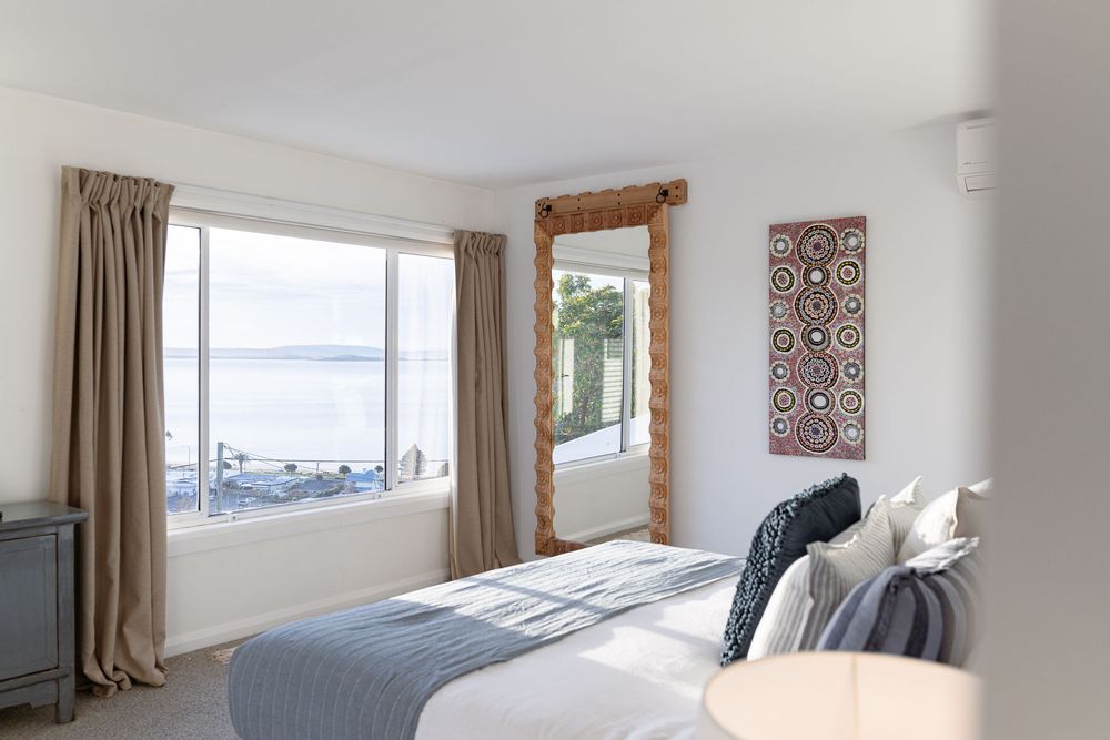 Contemporary bedroom with white walls, brown curtains, and decorative wall art featuring ocean views.