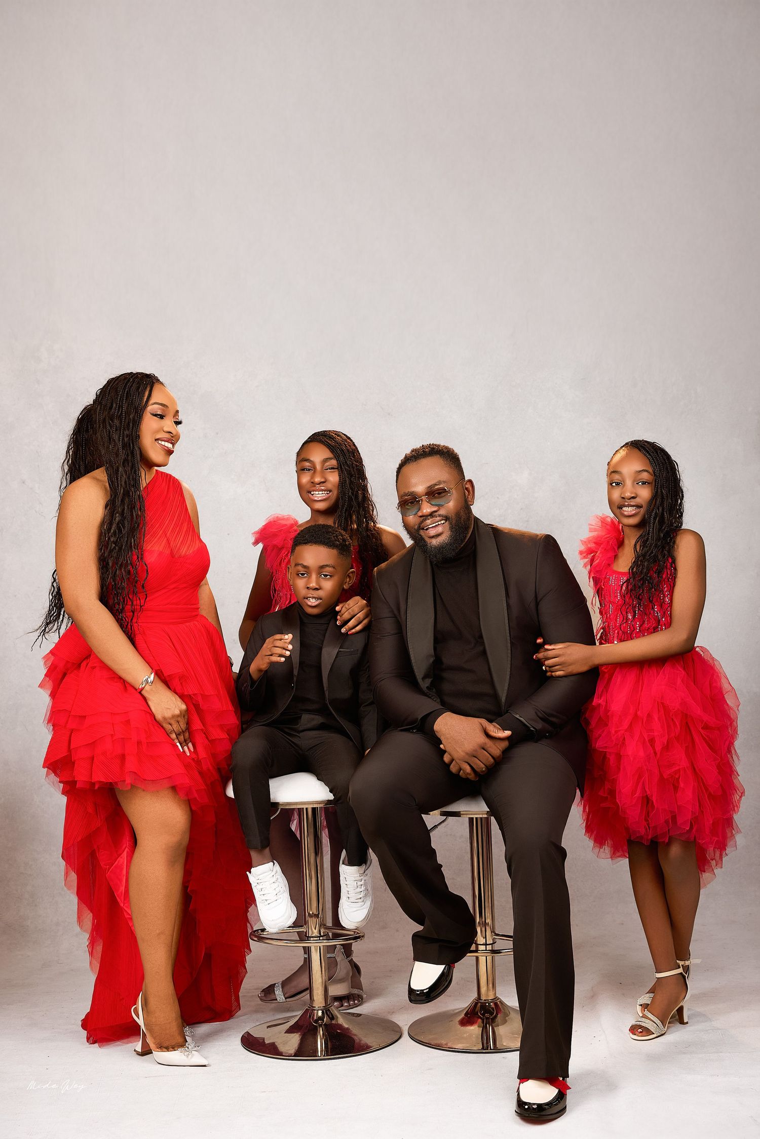 Family wearing coordinating red outfits poses together for holiday portrait against white background.