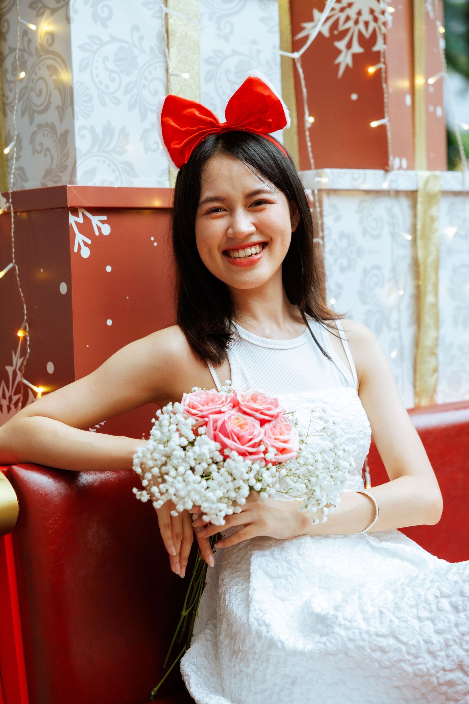 Person in white dress with red bow holding pink and white bouquet against decorative background.