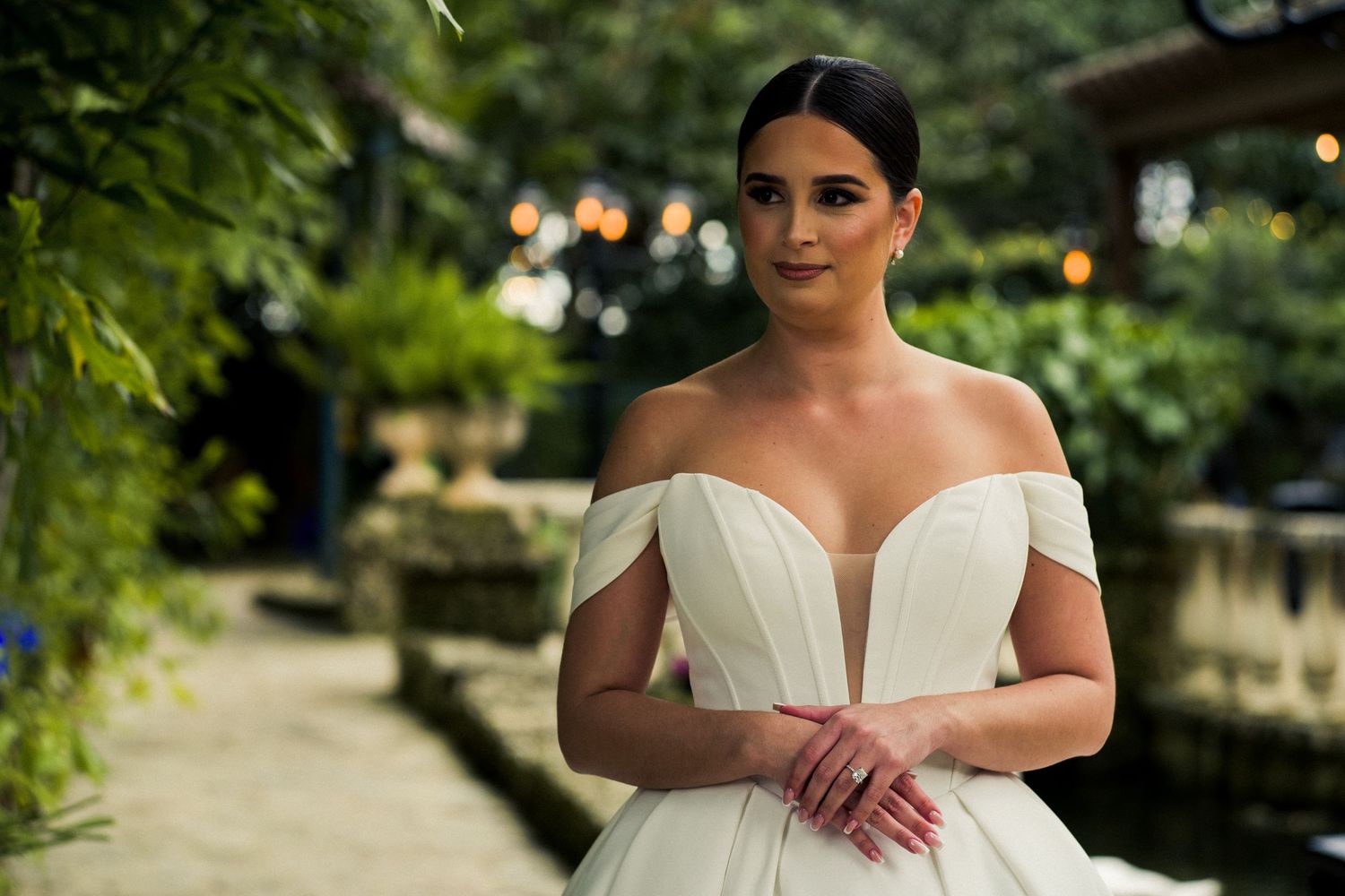 A bridal portrait in an elegant off-shoulder gown amid garden greenery.