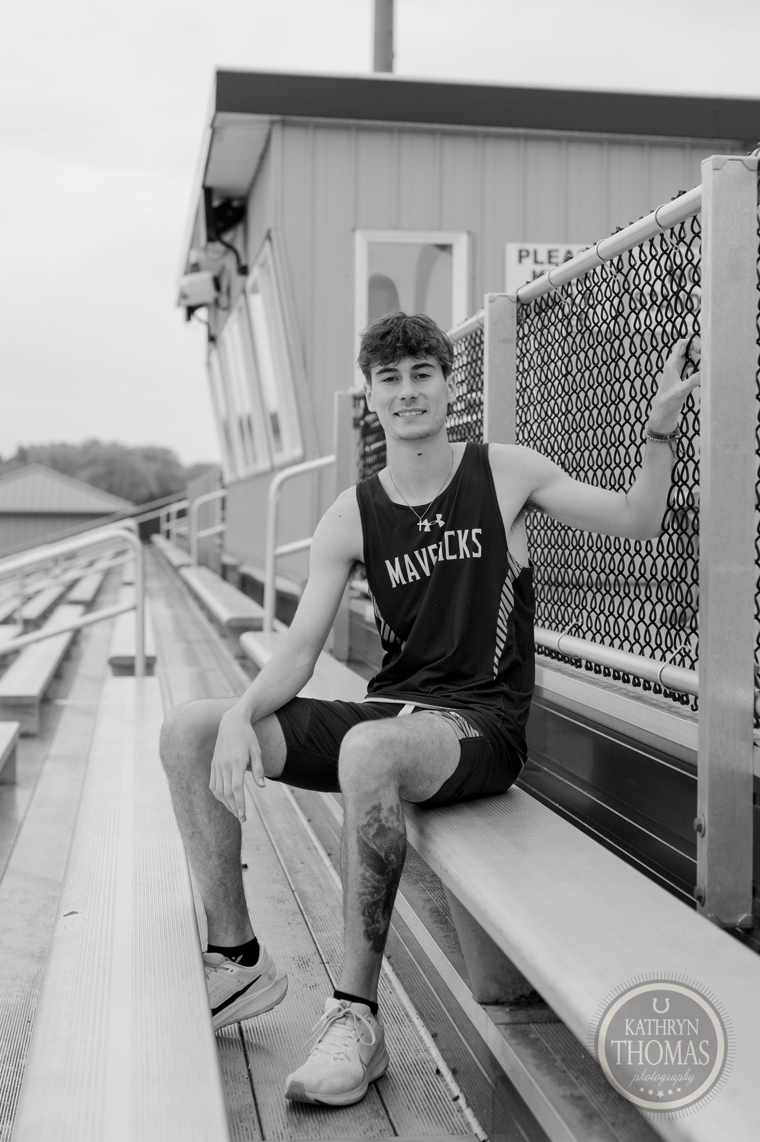Athletic graduate in black Mavericks uniform sits casually on bleachers.