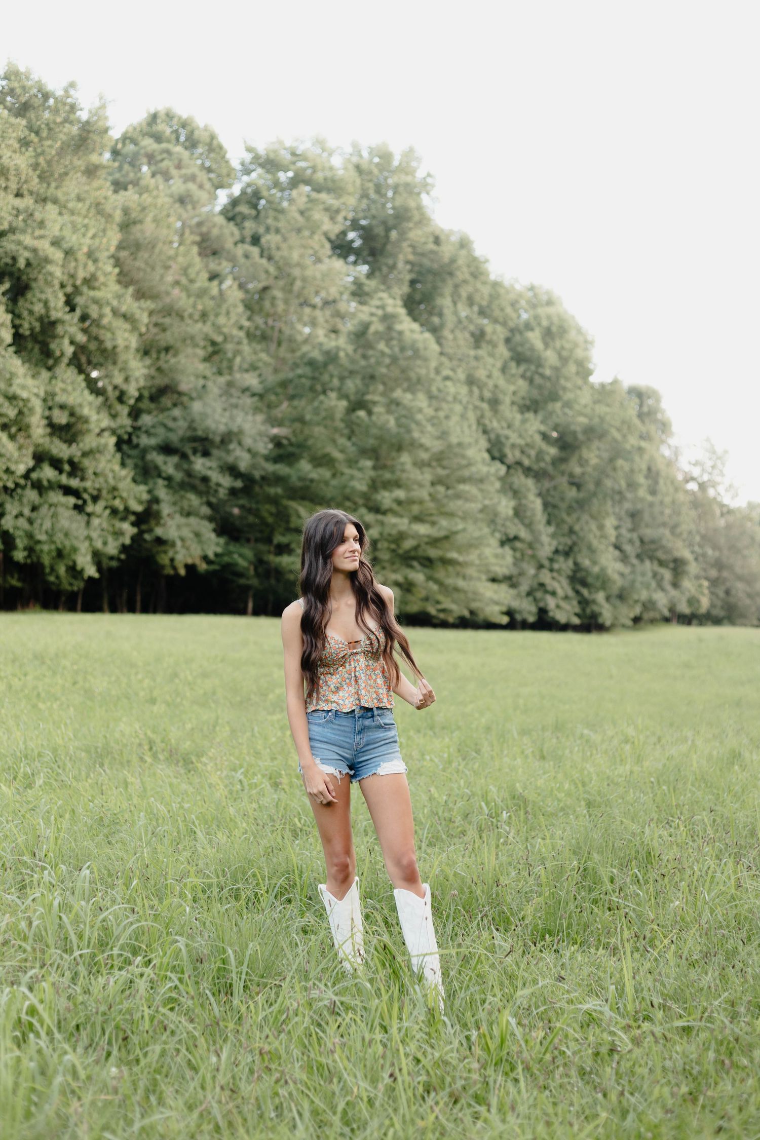 Woman in western boots and denim shorts standing in sunny meadow.