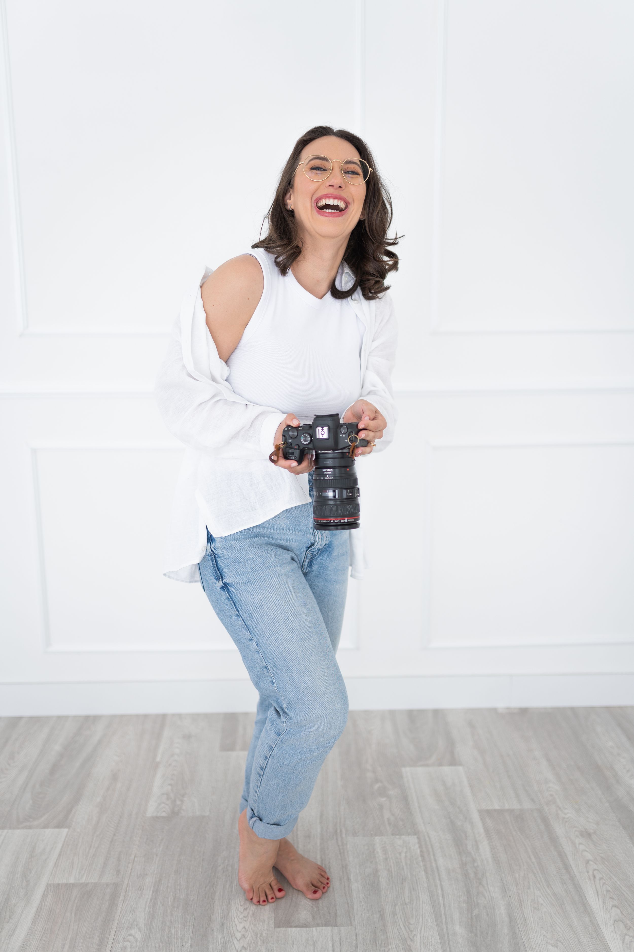 Professional portrait showing someone wearing glasses and a white sleeveless wrap top against a plain background.