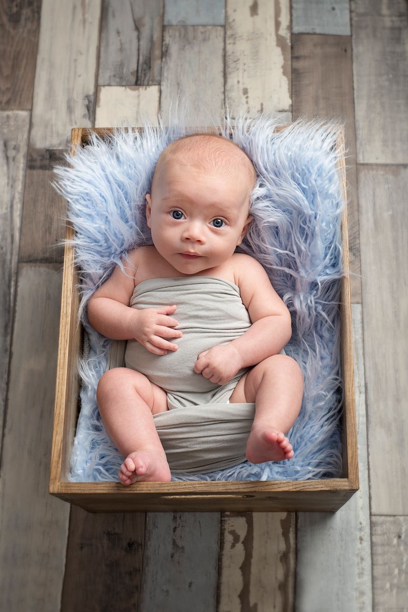 4 month boy wrapped in blue blanket in wooden crate