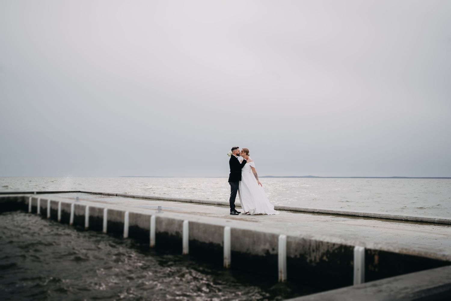Minimalist wedding photos on wooden pier extending into misty waters.