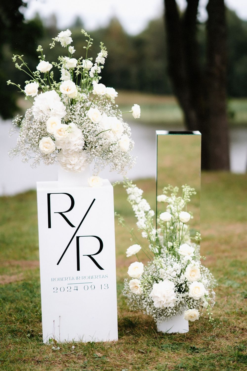 White floral arrangements and monogram signs decorate a grassy outdoor wedding venue.