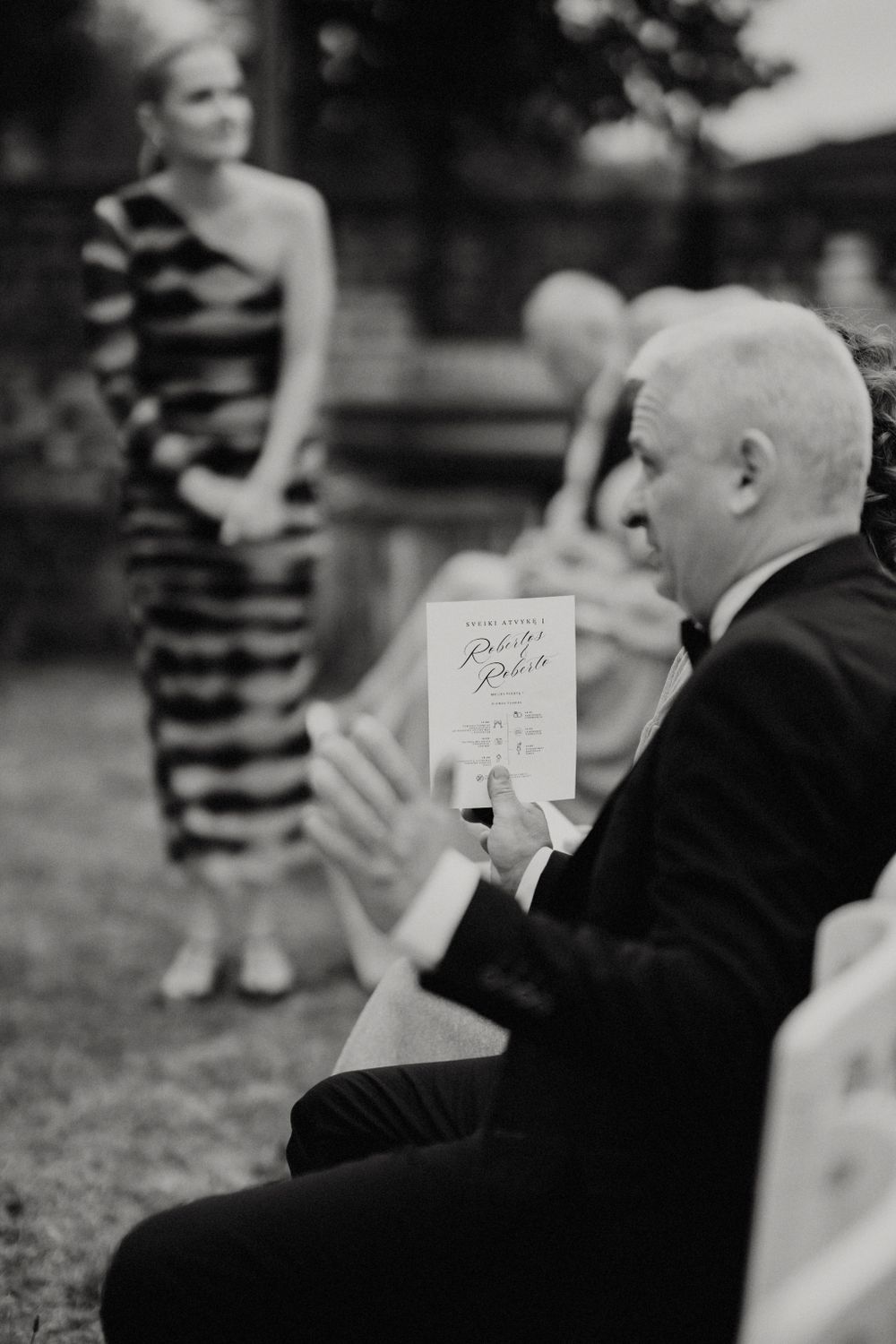 Wedding guests seated in white chairs view the ceremony program.