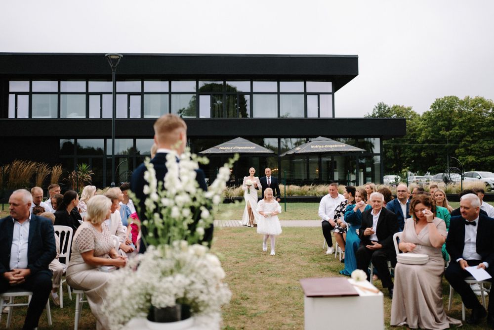 Outdoor wedding ceremony with white chairs and floral decorations under cloudy skies.