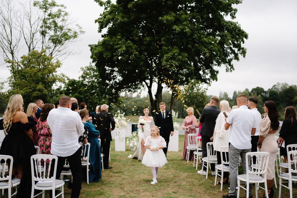 Wedding ceremony site with white chairs arranged in rows under mature trees.