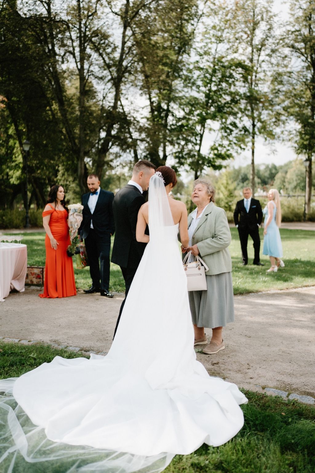 Elegant outdoor wedding scene with flowing white bridal gown train against natural greenery.