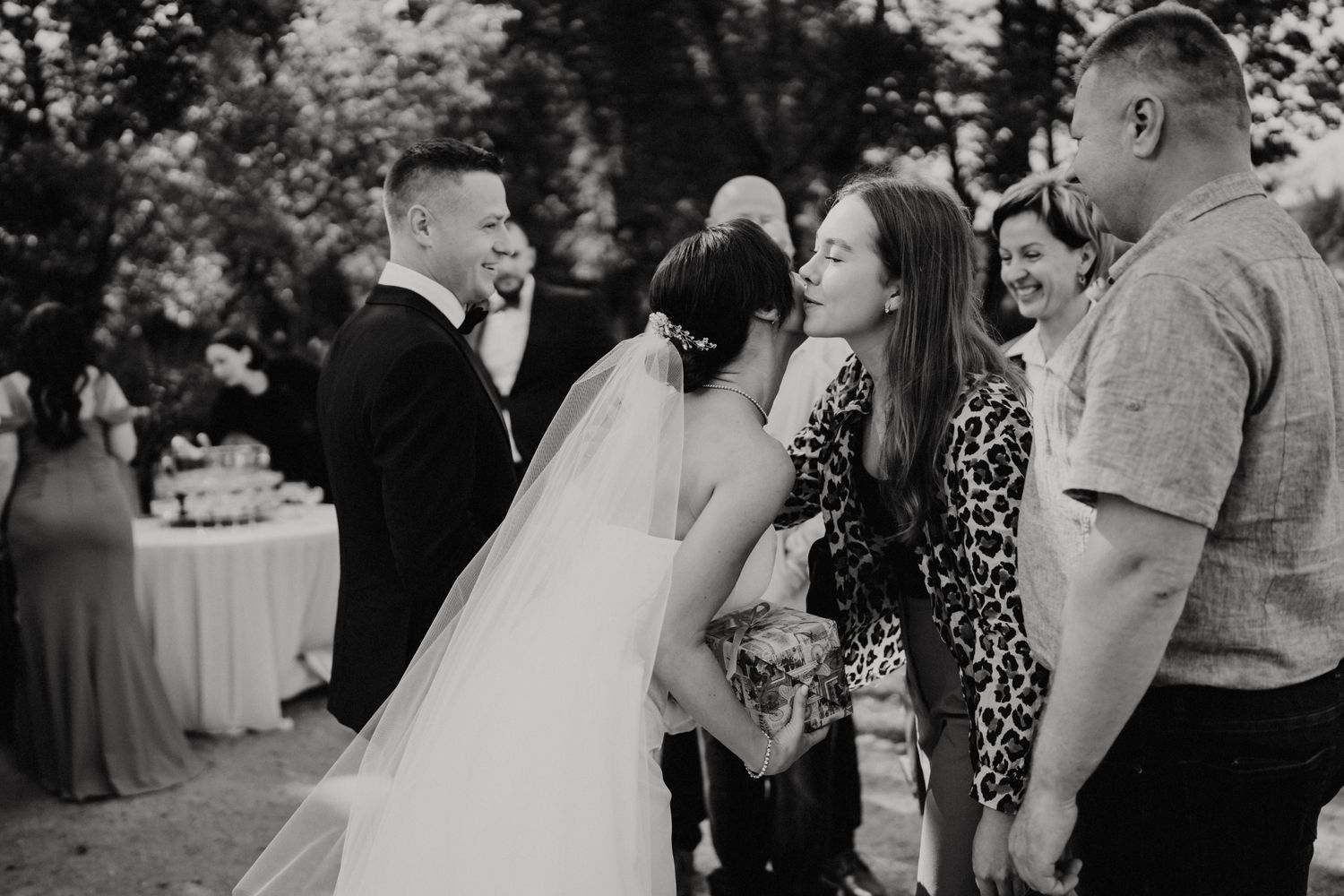 Black and white candid moment of wedding guests laughing together at outdoor reception.