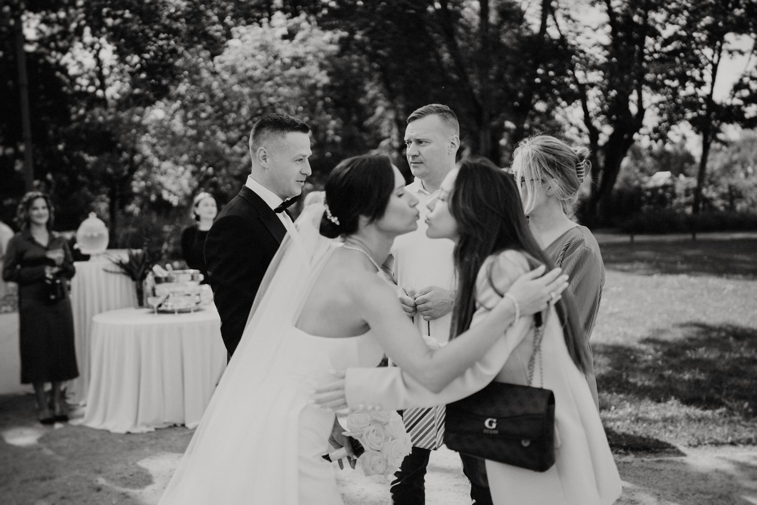 Black and white candid shot of wedding guests sharing joyful moment at outdoor reception.