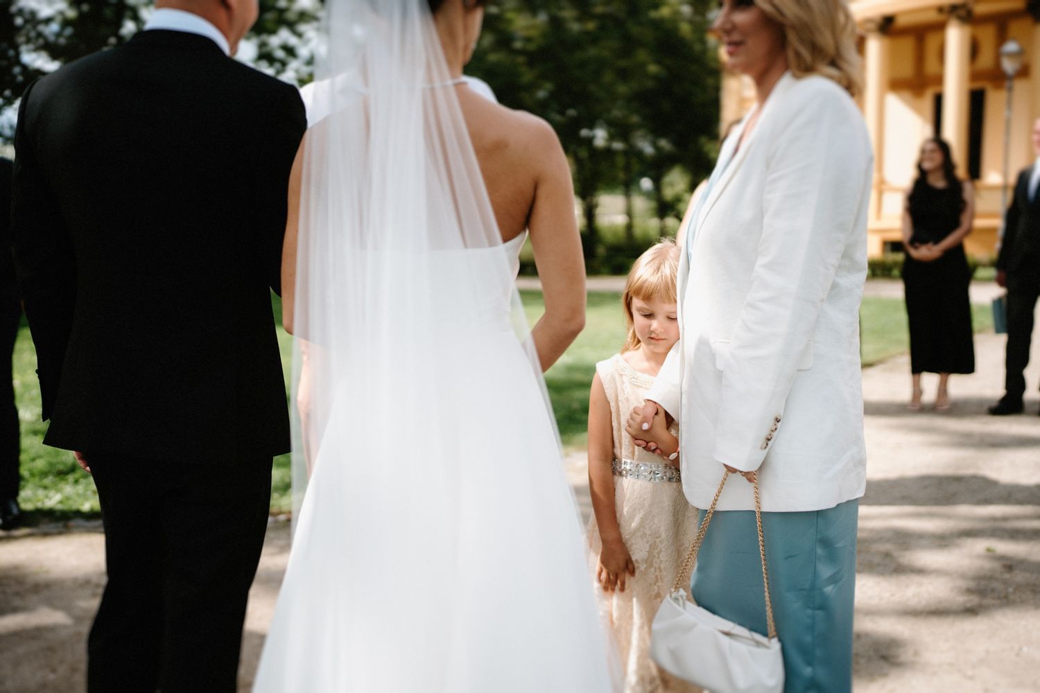 Wedding party gathered on garden path with elegant white bridal gown in focus.