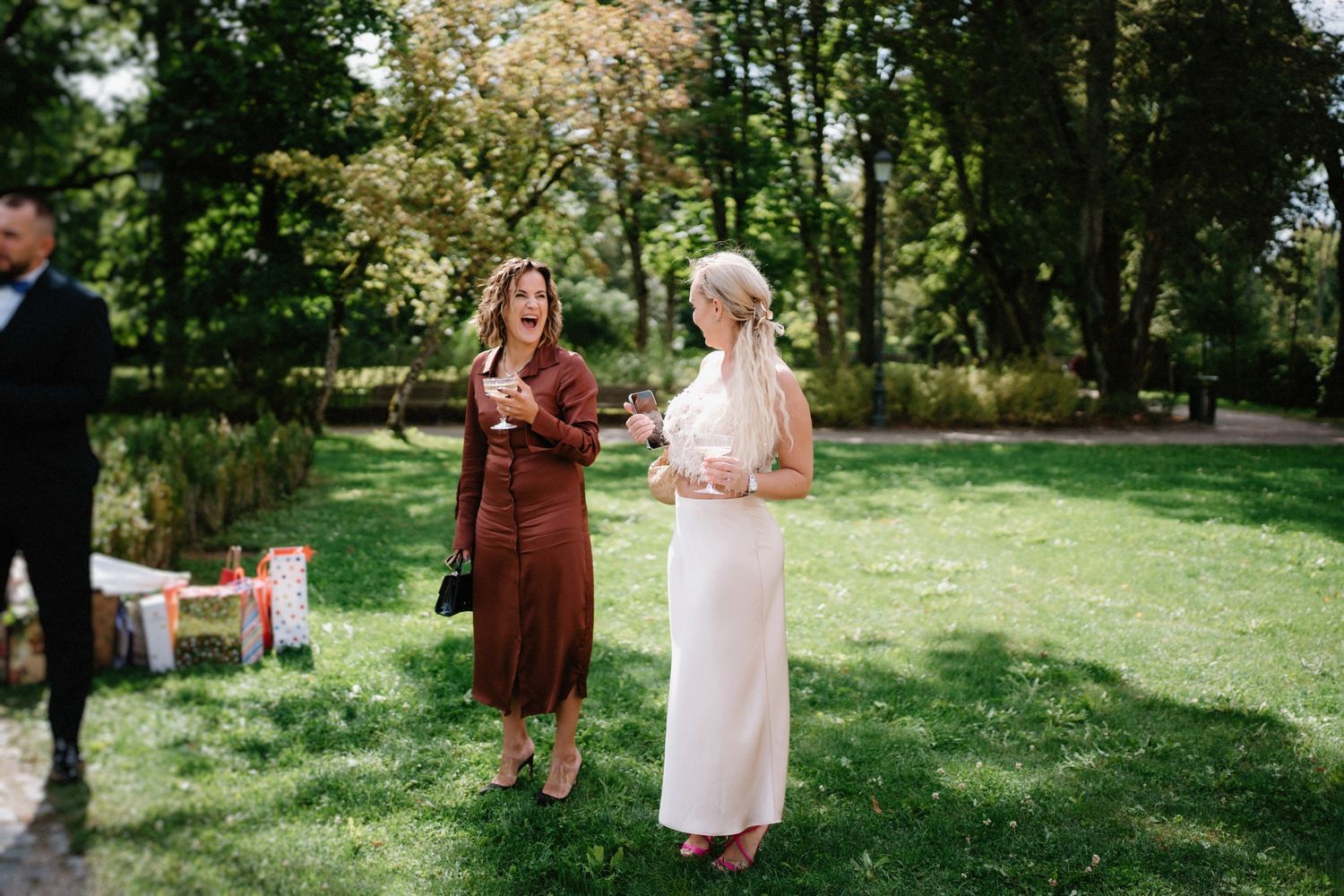 Wedding guests gather on a sunny lawn surrounded by trees during an outdoor ceremony.
