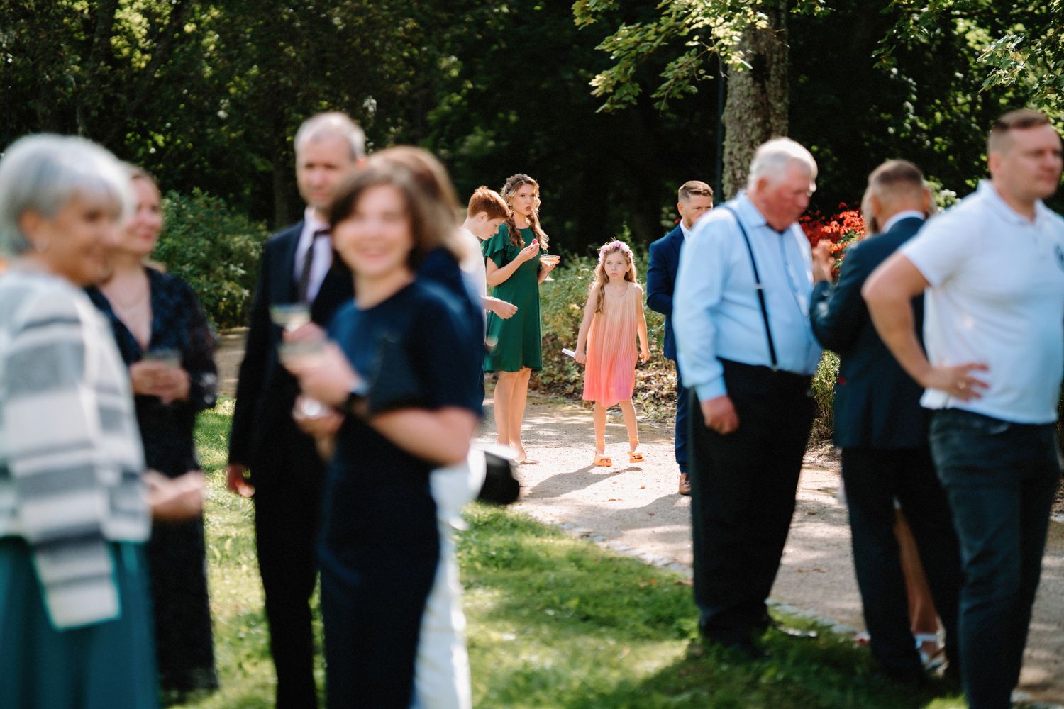 Wedding attendees socialize on a grassy lawn during a sunny outdoor reception.