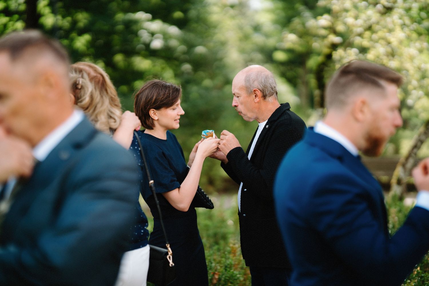 Wedding party members stand in formal attire against a natural outdoor backdrop.