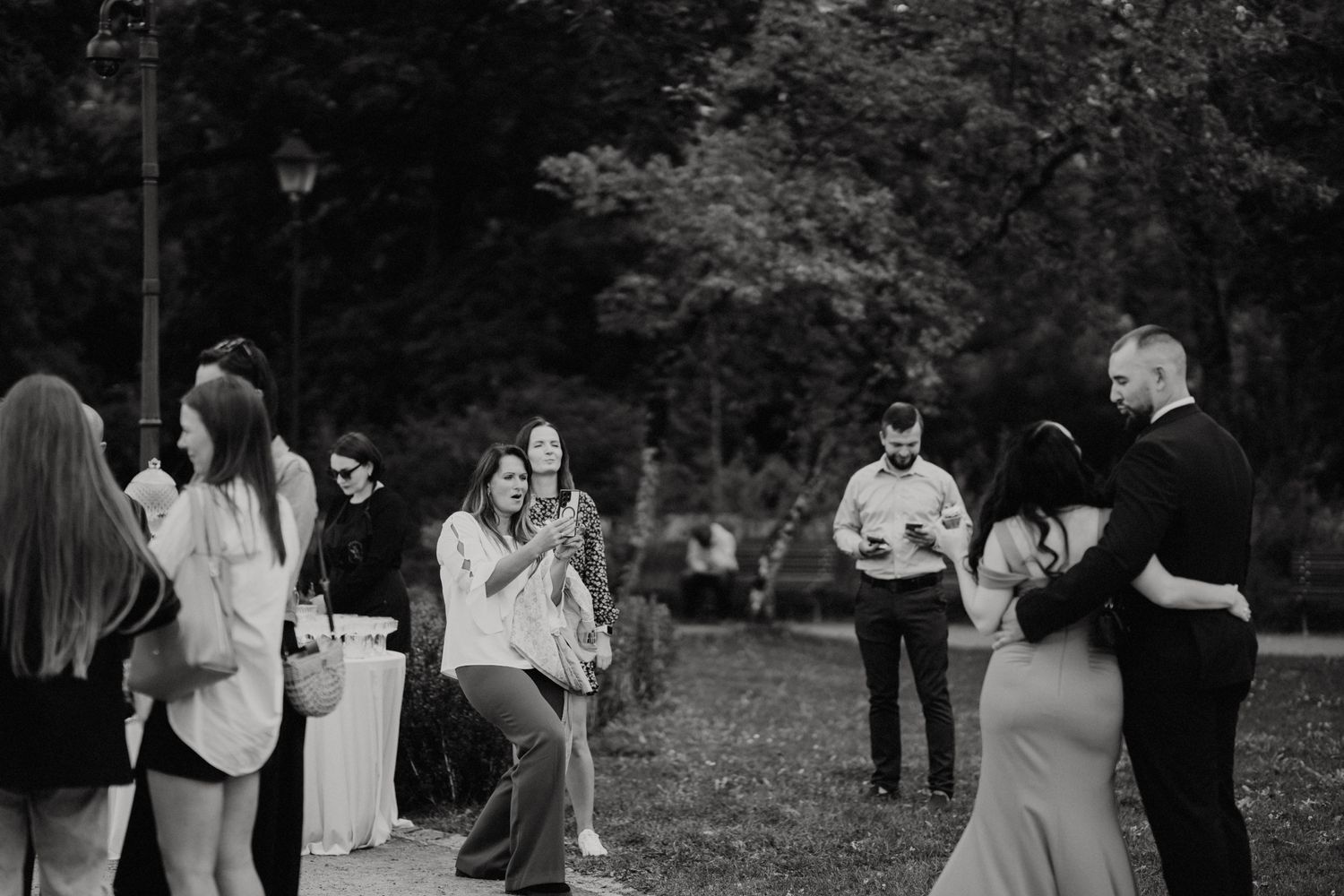 Black and white image of wedding guests mingling at an outdoor reception.