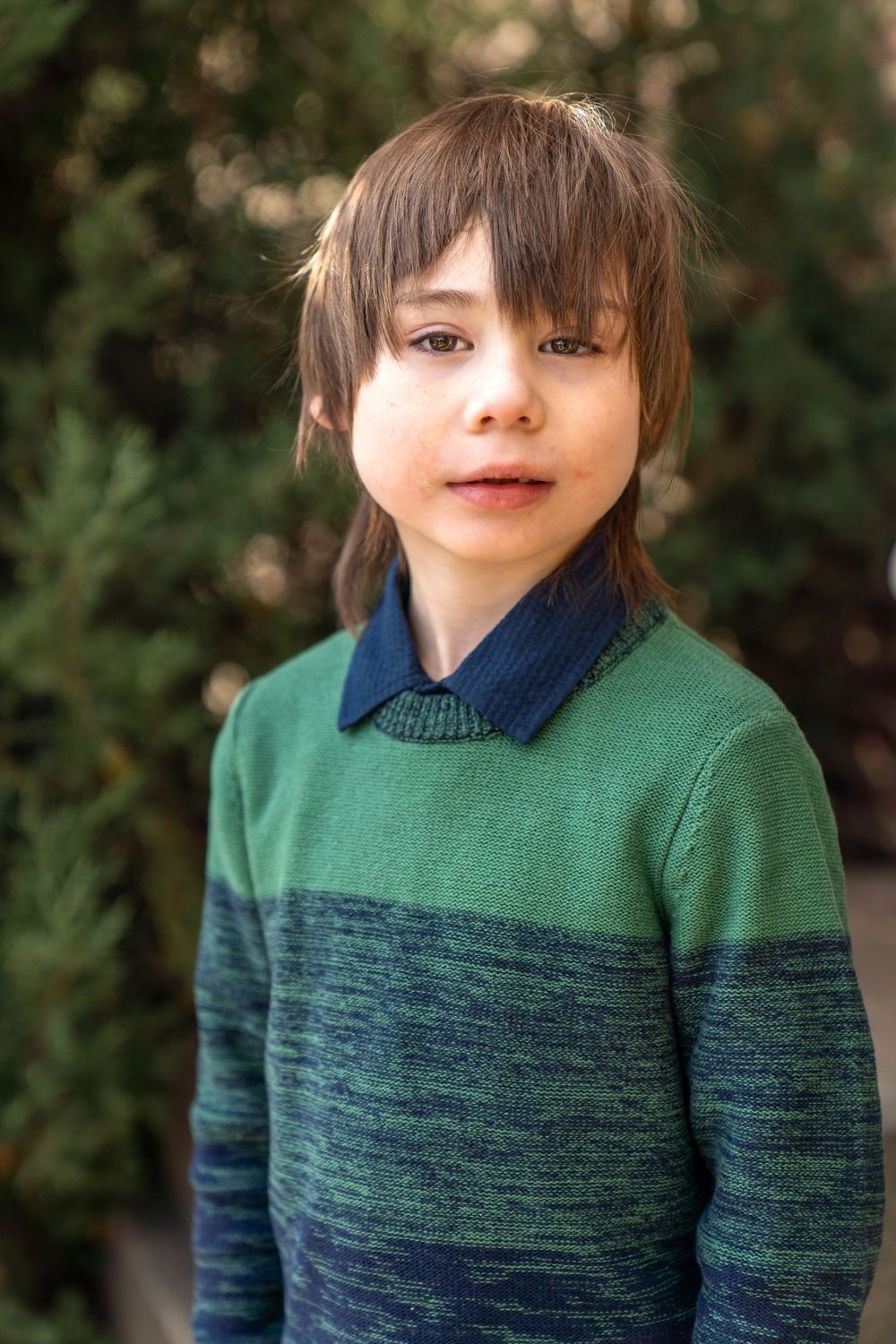 Child wearing a green and navy color block sweater outdoors.