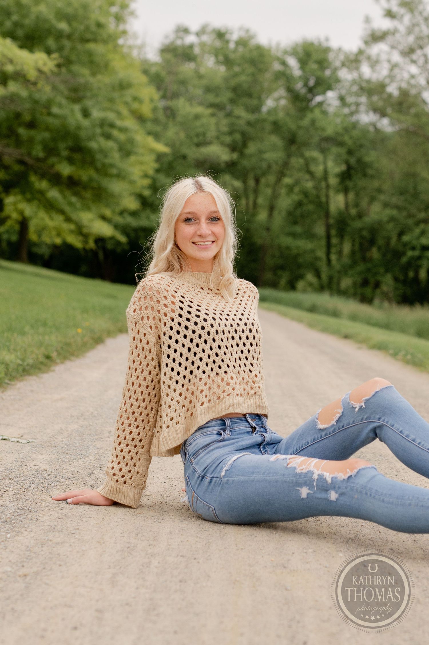 Relaxed lifestyle photo on a gravel path wearing a beige mesh sweater and ripped denim.