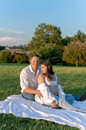 Couple relaxing on white blanket in grassy field during golden hour.