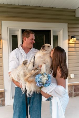 Golden retriever being held up between couple on front porch with blue flowers.