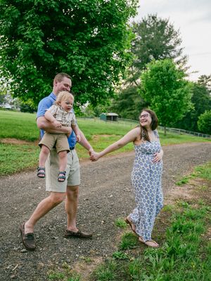 Family enjoying a playful moment together on a dirt path surrounded by lush green trees and grass on a summer day.