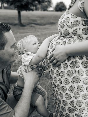 Black and white portrait of a toddler touching a pregnant woman's belly while a man leans in close.