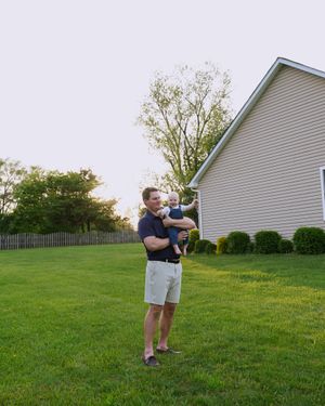 A tender backyard moment against a suburban house with well-maintained green lawn and fence.