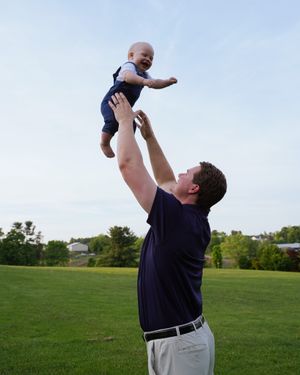 Playful moment of lifting a baby high in the air against a blue sky in a grassy backyard.