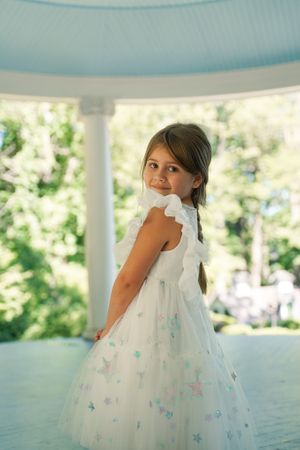 A young girl poses in a white dress with butterfly details in a gazebo.