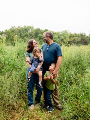 A family shares a joyful moment together while standing in a lush green meadow on a sunny day.