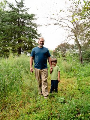 Two people standing together on a grassy path surrounded by lush green vegetation and trees on a bright day.