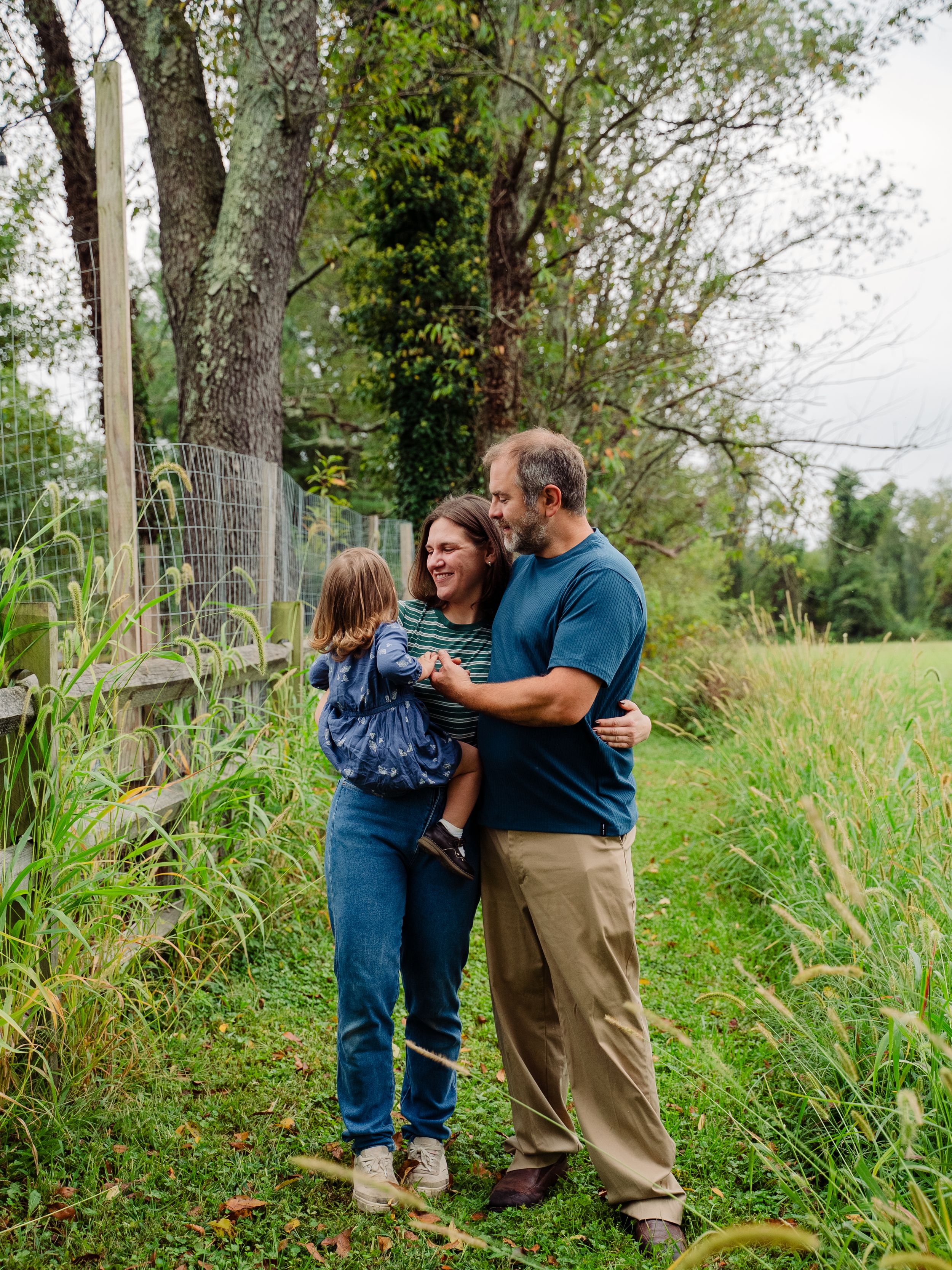 Family sharing tender moments together in a natural outdoor setting with tall grass and trees.