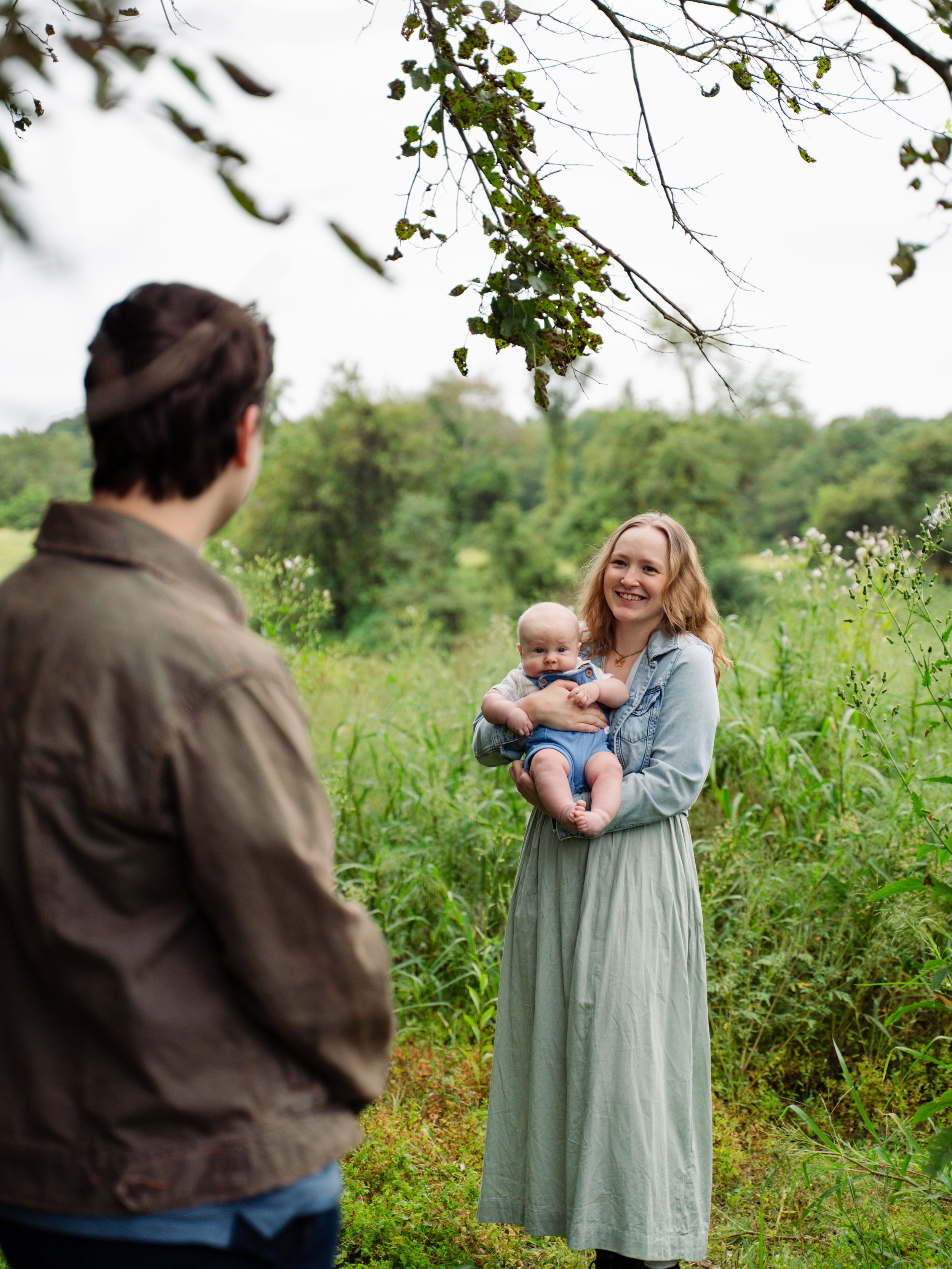 A group of people gather outdoors in a natural setting with greenery and trees in the background.